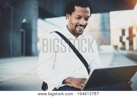 Happy African American man working with electronic touch pad pro with holding in hands.Concept of guy using Internet-enabled electronic device outside.Blurred background.Cropped