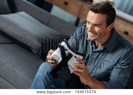 Cool toy for big guy. Quick witted dynamic fashionable guy choosing the mode while sitting on the couch and getting ready for his VR experience