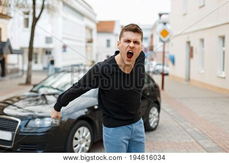 Angry Man Screams Near A Car In The City. The Concept Of Anger