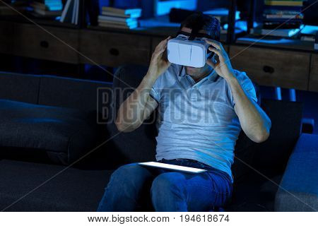 Diving in another world. Passionate nice enthusiastic man sitting on a couch and setting up the device for exploring another reality through game