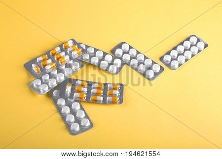 Many different pills, vitamins, tablets, dose, medicine, pilule and drugs on yellow background. Medicinal tablets. White and yellowt pills in packaging are scattered.