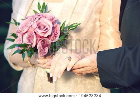 Middle-aged couple holding hands, woman holding bouquet, mid-section, close-up of hands