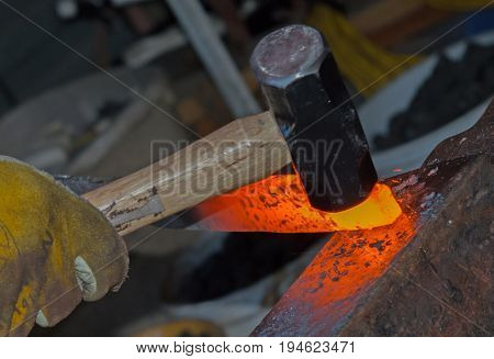 The bladesmith exhibits his skills by precisely hammering the heated metal to shape it into a knife blade. Photographed with a bokeh background effect.