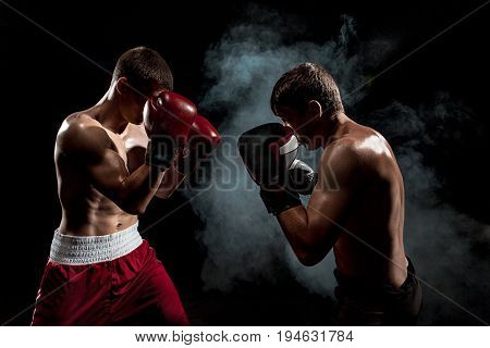 Two professional boxer boxing on black smoky studio background.