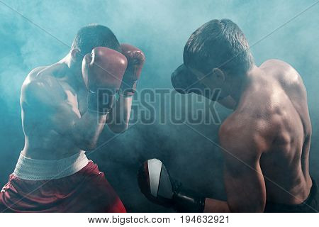 Two professional boxer boxing on black smoky studio background.