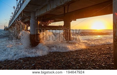 Waves smite upon the pier support at sunset