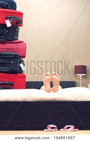 Low section of woman lying down in bed next to stack of suitcases