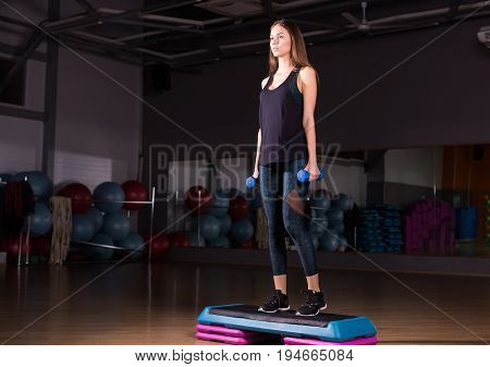 Fitness step, training, aerobics, sport concept - Athletic woman trainer at step doing aerobic with steppers indoors. Fitness woman with step platform doing workout