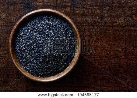 Black Sesame Seeds In Dark Wooden Bowl Isolated On Dark Brown Wood From Above.