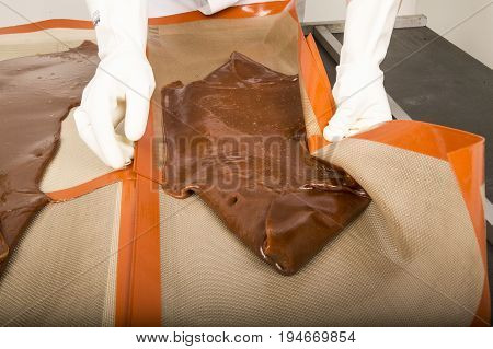 Artisanal production of caramel toffee sweets butterscotch candies. Woman with white lab coat blouse stretching moving extending the sugar pastry to do butterscotch candies sweet of France