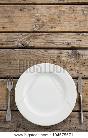 Overhead view of empty plate amidst fork and table knife on wooden table