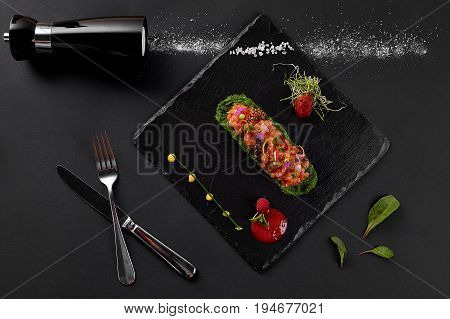 fresh salmon tartar with salt and herbs, studio shot. Fish tartar on black shale. Top view.