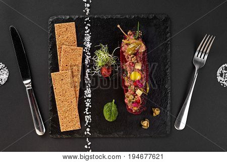 fresh beef tartar with salt and herbs and Crispbread, studio shot. Meat tartar on black shale. Top view