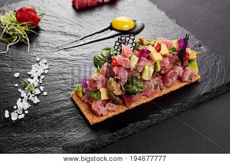 fresh tuna tartar with salt and herbs, studio shot. Fish tartar on black shale