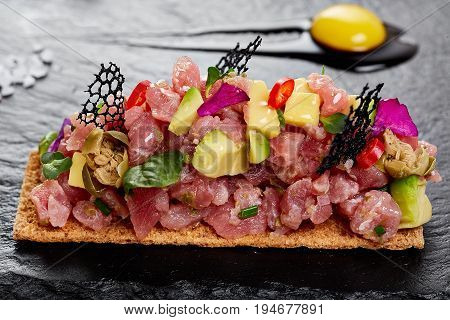 fresh tuna tartar with salt and herbs, studio shot. Fish tartar on black shale