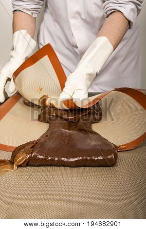 Artisanal production of caramel toffee sweets butterscotch candies. Woman with white lab coat blouse stretching moving extending the sugar pastry to do butterscotch candies sweet of France
