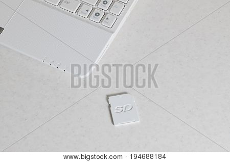A Compact Sd Memory Card Lies On A White Netbook. The Digital Information Storage Device Is Ready Fo