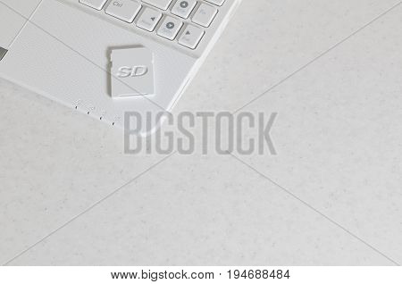 A Compact Sd Memory Card Lies On A White Netbook. The Digital Information Storage Device Is Ready Fo