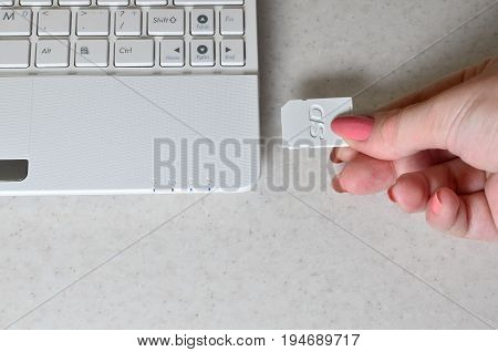 A Female Hand Inserts A White Compact Sd Card Into The Corresponding Input In The Side Of The White