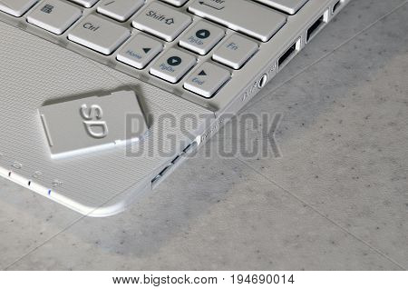 A Compact Sd Memory Card Lies On A White Netbook. The Digital Information Storage Device Is Ready Fo