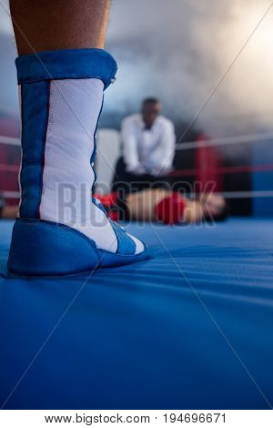Low section of boxer standing against referee by athlete lying in boxing ring