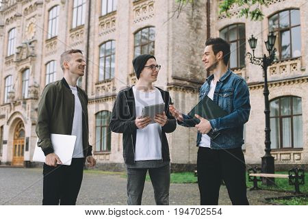 Three delighted students have a break at the college. They went outside to relax after hard day. Smart boys talking about their girls