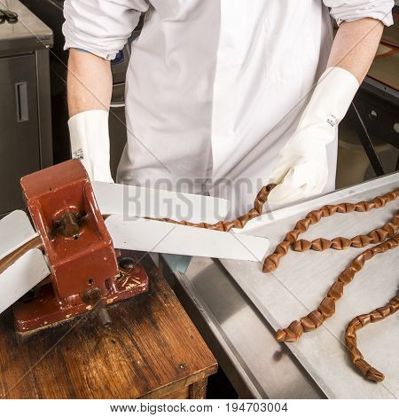 Artisanal production of caramel toffee sweets butterscotch candies. Woman with white lab coat blouse cutting rolls of sugar pastry to do butterscotch candies traditional sweetx of France