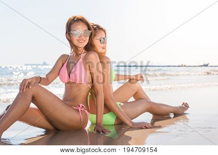 Two sexy women in bikinis on the sunny beach. Best friends having fun Summer vacation holiday lifestyle. Happy women relaxing freedom on white sand.