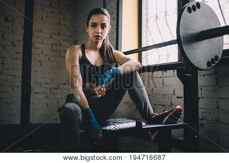 Confident and concentrated young female looking at the camera and resting on the powerlifting machine with placed leg on the top