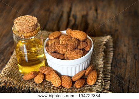 Close up almond oil in the bottle and almond seed in white cup for oil massage and spa treatment ingredient on wooden table background