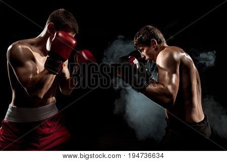 Two professional boxer boxing on black smoky studio background.