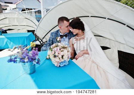 Beautiful Wedding Couple Enjoying Each Other's Comany On A Bench On A Lakeside.
