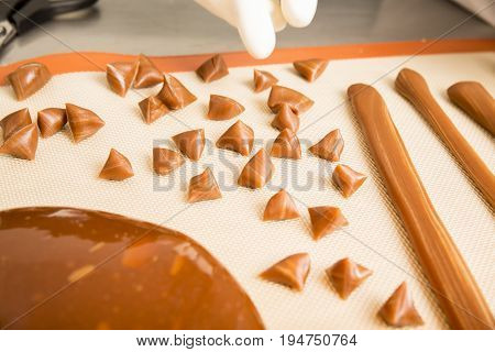 Artisanal production of caramel toffee sweets butterscotch candies. Woman with white lab coat blouse cutting rolls of sugar pastry to do butterscotch candies traditional sweetx of France