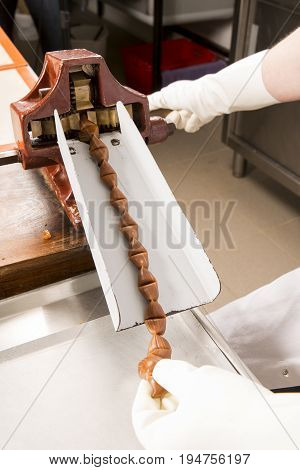 Artisanal production of caramel toffee sweets butterscotch candies. Woman with white lab coat blouse cutting rolls of sugar pastry to do butterscotch candies traditional sweetx of France