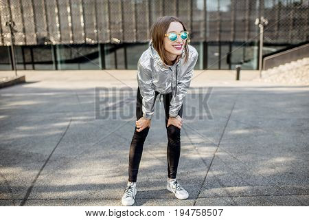 Lifestyle portrait of a stylish woman in silver jacket exersicing outdoors in the modern urban environment