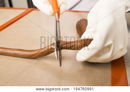 Artisanal production of caramel toffee sweets butterscotch candies. Woman with white lab coat blouse cutting rolls of sugar pastry to do butterscotch candies traditional sweetx of France