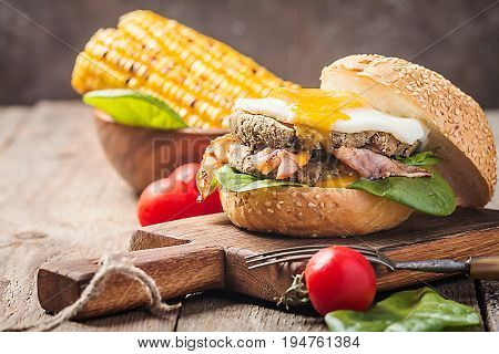 Homemmade Bacon Hamburger with fried Egg, Lettuce and lentil burger with a garnish of corn and tomatoes