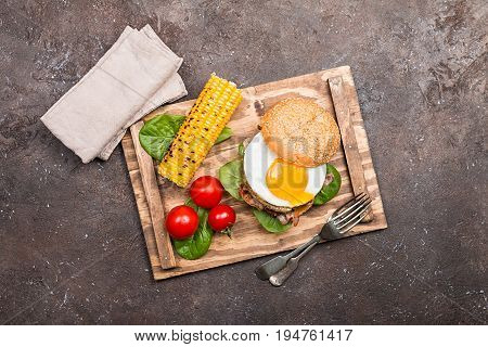 Homemmade Bacon Hamburger with fried Egg, Lettuce and lentil burger with a garnish of corn and tomatoes, top view