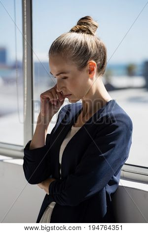Thoughtful businesswoman looking lown while standing by window in office
