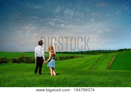 Young Couple Standing On Green Field, Woman Showing Her Hand At The Stars