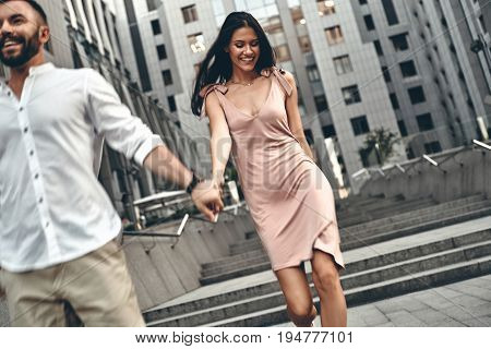 Enjoying carefree walk. Beautiful young couple holding hands and smiling while walking down the stairs outdoors
