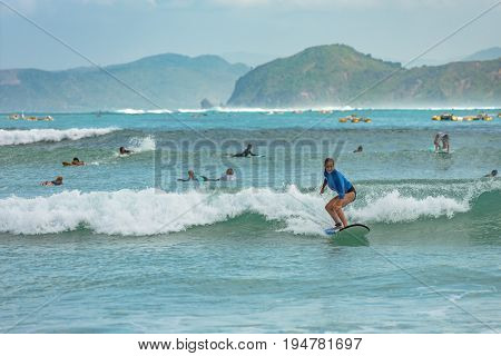 10/06/2017 Pantau Mawun Lombok Indonesia. Young woman learns to surf on a long board on learner waves in a paradise location.