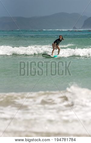 10/06/2017 Pantau Mawun Lombok Indonesia. Young woman learns to surf on a long board on learner waves in a paradise location.