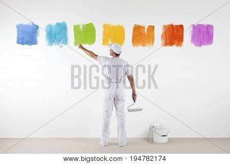 Rear view of painter man pointing with finger the colors on wall with paint roller and bucket isolated on white