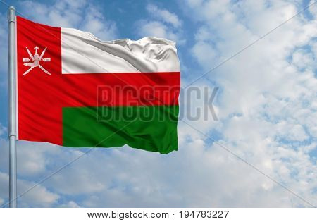 National flag of Oman on a flagpole in front of blue sky.