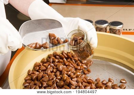 Artisanal production of caramel toffee sweets butterscotch candies. Woman with white gloves shaking put in jar get in the jugs the pieces of butterscotch candies traditional sweets of France