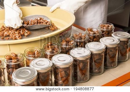 Artisanal production of caramel toffee sweets butterscotch candies. Woman with white gloves shaking put in jar get in the jugs the pieces of butterscotch candies traditional sweets of France