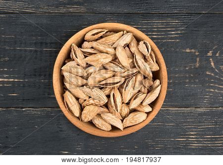 Uzbek inshell almonds in a bowl on wooden background, top view