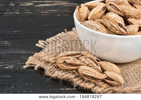 Uzbek inshell almonds in bowl on a burlap and wood background closeup