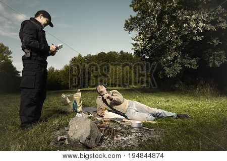 Vagabond young man checked by police patrol near illegal fireplace
